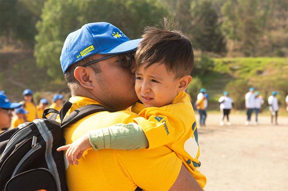 Un padre de familia cargando a su hijo menor en un voluntariado de reforestación.